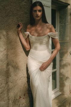 a woman in a white dress leaning against a wall