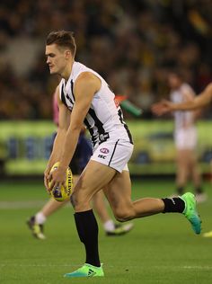 a male afl player is running with the ball in his hand and other players are on the field behind him