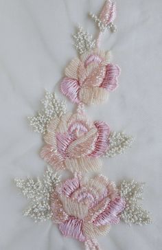 three pink and white flowers with pearls on them sitting on top of a table cloth