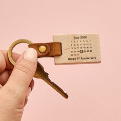 a person holding a wooden keychain with a date stamp on it and a leather key chain