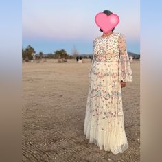 a woman with a heart shaped balloon on her head standing in the middle of an empty field