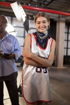 a woman standing with her arms crossed in front of a camera and another man behind her