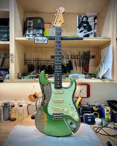 a green electric guitar sitting on top of a wooden table in a room filled with tools