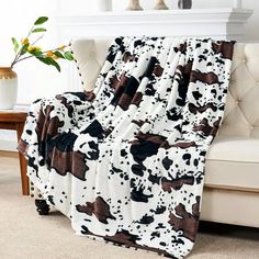 a cow print blanket sitting on top of a couch next to a vase with flowers