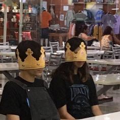 two people wearing crowns sitting at a table in a restaurant with tables and chairs behind them