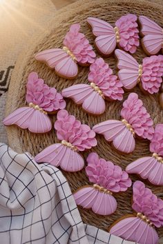 pink decorated cookies sitting on top of a wicker basket next to a white and black checkered cloth