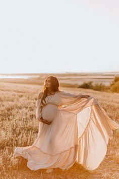 a pregnant woman in a white dress is walking through a field with her long flowing fabric