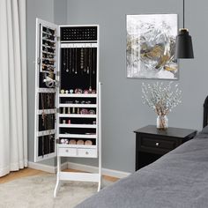 a white jewelry cabinet in a bedroom next to a bed