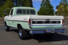 an old pick up truck parked in a parking lot with trees in the back ground