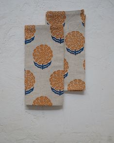 two napkins with orange flowers on them against a white wall, one is folded and the other has blue stripes