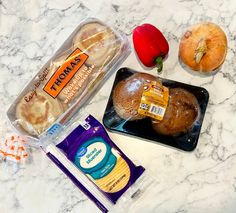 an assortment of breads and vegetables on a marble counter top with plastic wrappers