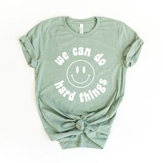 Looking for a cute versatile top to wear this summer? Make sure to grab one of our We can Do Hard Things Smiley Face tees! This soft and comfortable graphic tee is the perfect top for any outfit. It can be paired with biker shorts, jeans, or even a simple skirt/dress! This tee is true-to-size, so be sure to order your regular t-shirt size! If you are looking for a more oversized look, make sure to size up! Graphic Tees For Teachers, Slp Shirt Designs, Casual Slogan Top With Comfortable Fit, Green Summer Shirt With Slogan, Green Casual Tops With Funny Print, Casual Green Tops With Funny Print, Casual Tops With Funny Print For Everyday, Comfortable Slogan Tops For Summer, Comfortable Fit Slogan Tops For Summer