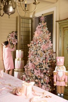 a pink christmas tree in the middle of a room with decorations on it and a woman standing next to it