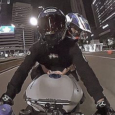 two people riding on the back of a motorcycle down a city street at night with buildings in the background