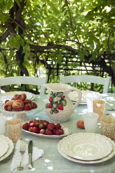 the table is set with plates and bowls of strawberries