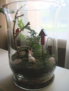 a glass vase filled with plants and animals on top of a white table next to a window