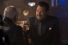 a man in a star trek uniform is talking to another man who is holding a drink