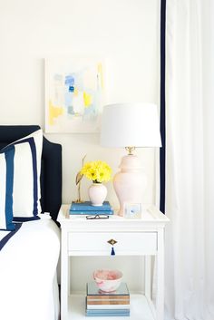 a white nightstand with yellow flowers and books on it next to a blue chair in a bedroom