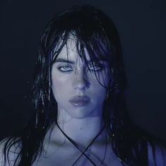 a woman with wet hair and blue eyes is posing for the camera in dark lighting