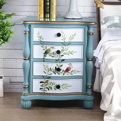 a painted chest of drawers next to a bed with a plant and books on it