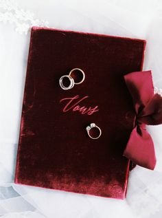 two wedding rings sitting on top of a red velvet book with the word vows written in cursive writing