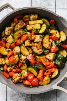 a pan filled with vegetables and chicken on top of a tile floor next to a wooden spoon