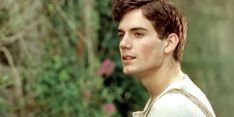 a young man is standing in front of some bushes