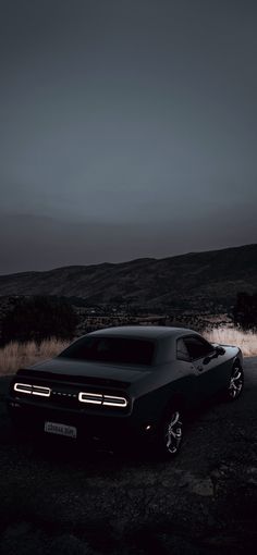 a black car parked on the side of a road in front of a hill at night