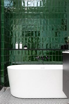 a green tiled bathroom with a white bathtub