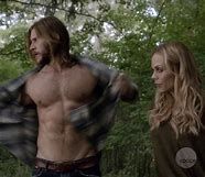 a shirtless man standing next to a woman in the woods