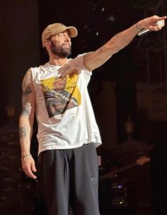 a man with tattoos on his arm pointing at something in the air while standing on a stage