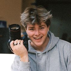 a young man holding up a camera in front of his face and smiling at the camera