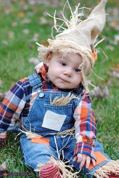 a little boy sitting in the grass wearing a scarecrow hat and overalls,