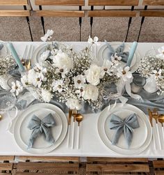 the table is set with white and blue flowers, silverware, and napkins