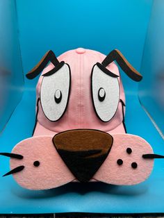 a pink hat with a dog's face on the front and side, sitting on top of a blue chair