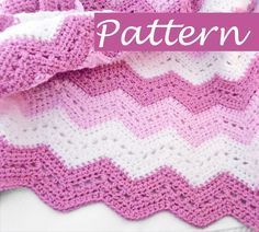 a pink and white crocheted blanket laying on top of a bed next to a pillow