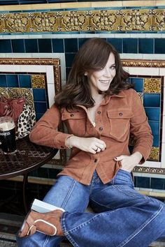 a woman sitting on top of a wooden bench next to a wall with blue tiles