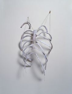 an artistic sculpture made out of strips of white paper hanging from strings on a gray wall