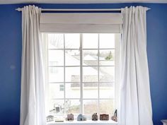 a bedroom with blue walls and white drapes on the window sill in front of it