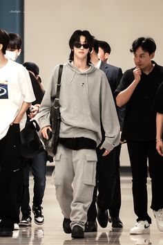 a man in grey sweatshirt and pants walking through an airport with other people behind him