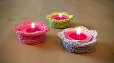 three crocheted baskets with candles in them on a wooden table, one is pink and the other is green