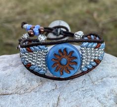 Blue Sun and Brown Leather Wrap Bracelet  The length of the bracelet is the inside circumference when the bracelet is clasped  This Bracelet Features 2mm Round Brown Genuine Leather A glass Blue Sun Bead 20mm Blue and Brown superduo beads (2 hole) beads 8/0 Silver seed beads Moon and Stars Button 17mm The Bracelet width is 1" at the widest point This Bracelet is so comfortable to wear it will really surprise you, and an excellent addition to any outfit! All Bracelets are hand made and are create Adjustable Beaded Cuff Bracelet For Beach, Blue Spiritual Wrap Bracelet For Festival, Handmade Blue Hippie Beaded Bracelets, Adjustable Beaded Blue Wrap Bracelet, Adjustable Blue Beaded Wrap Bracelet, Adjustable Nickel-free Blue Cuff Bracelet, Blue Beaded Leather Bracelet For Gift, Adjustable Blue Wrap Bracelet With Round Beads, Handmade Adjustable Round Wrap Bracelet