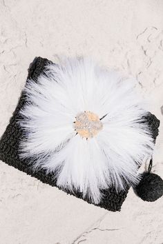 a black and white fur bag with a gold brooch on the front laying on sand