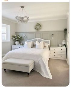 a white bed sitting in a bedroom next to a dresser and window with a chandelier above it