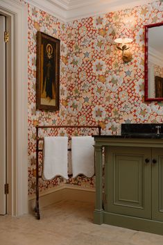 a bathroom with floral wallpaper and green cabinetry in the corner, along with an antique sink