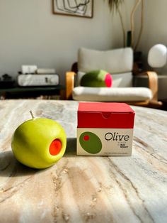 an apple sitting on top of a table next to a carton of olive juice