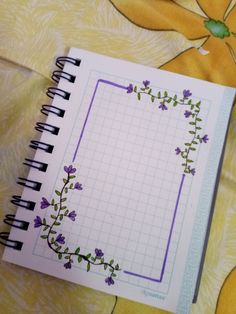 an open notebook with purple flowers and vines on the cover is sitting on a bed