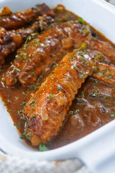 a white dish filled with meat covered in gravy and garnished with parsley