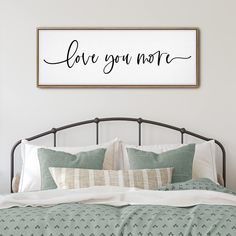 a bed with pillows and a framed sign above it that says love you more