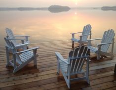 three adiron chairs sitting on top of a wooden dock next to a lake at sunset